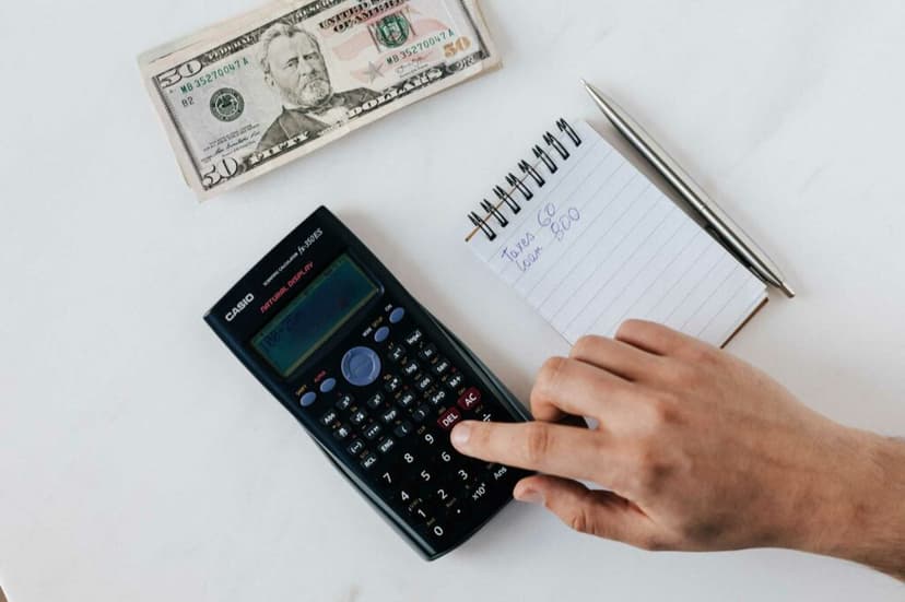 Finger pushing buttons on a calculator with money and a mini note pad to the right 