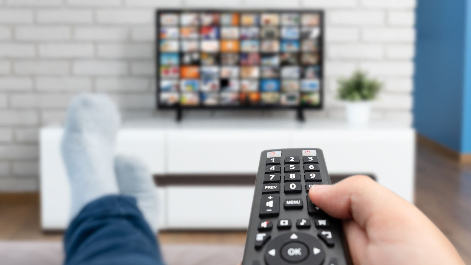 Person sitting on couch with feet up clicking on remote